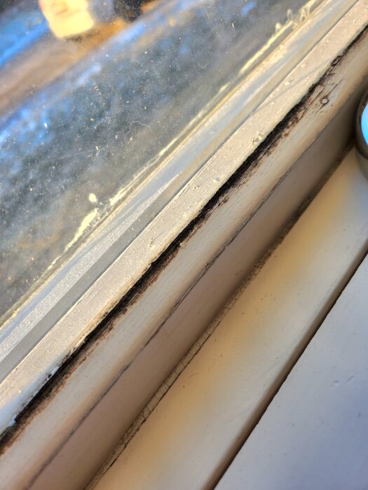 Mörka fläckar på ett fönsterkarm i närbild, möjligtvis mögel eller smuts.