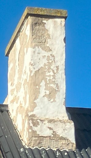 Renoverad tegelstensskorsten med flagnande silikatfärg efter två år, belägen på ett tak under klarblå himmel.