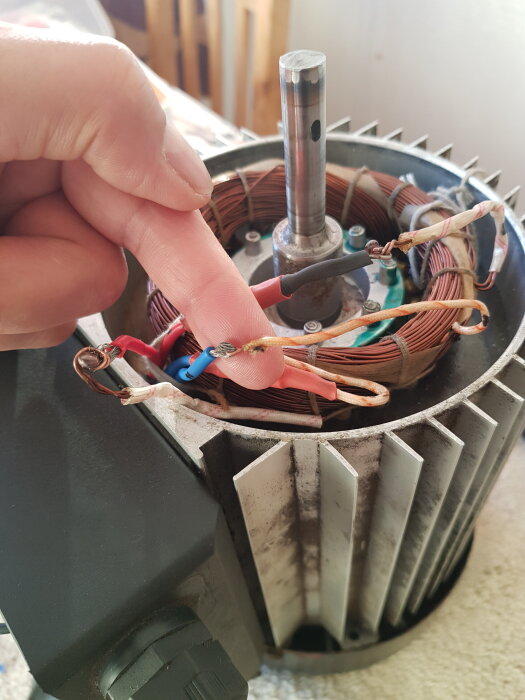 En hand pekar på kopparlindning och kablar i en öppen elmotor, vilket visar motorns inre detaljer.