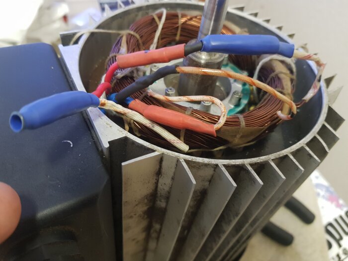 Närbild av en elektrisk motor med synliga kopparlindningar och kablar i olika färger, inklusive blå, röd och svart isolering på kablarna.