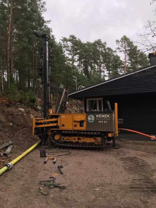 Borrigg utanför ett hus i skärgården, omgiven av tallar. Maskinen används för att borra brunnar för vattenförsörjning.
