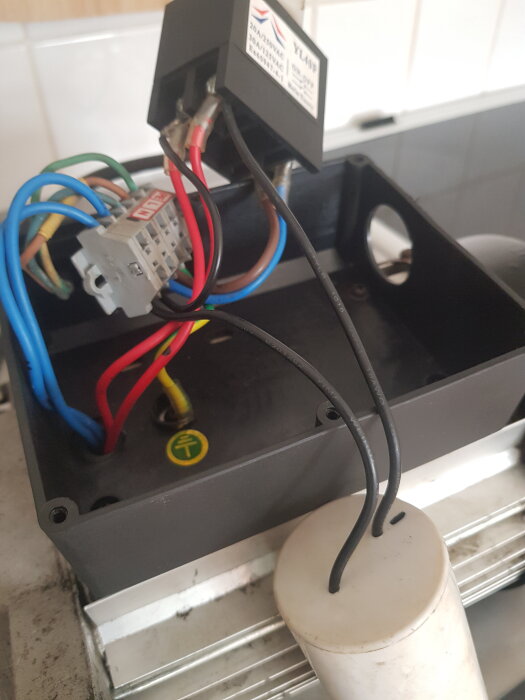 Kopplingsbox med anslutna färgade kablar och en vit kondensator i ett elektriskt projekt för motoranslutning.