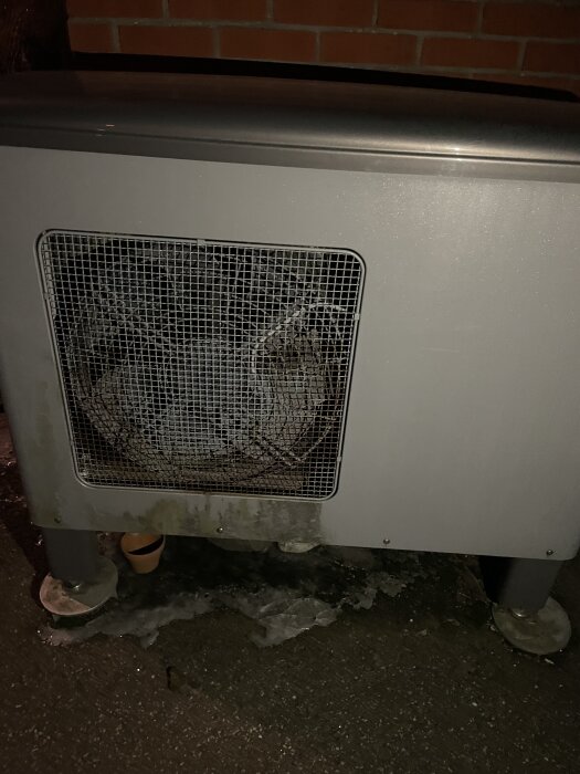 Utomhusdel av värmepump med isbildning och vattenläckage under enhet.