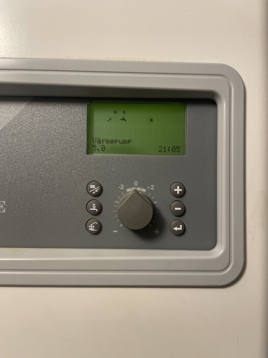 Styrpanel för värmepump med display som visar inställningar och tid, samt ratt och knappar för justering.