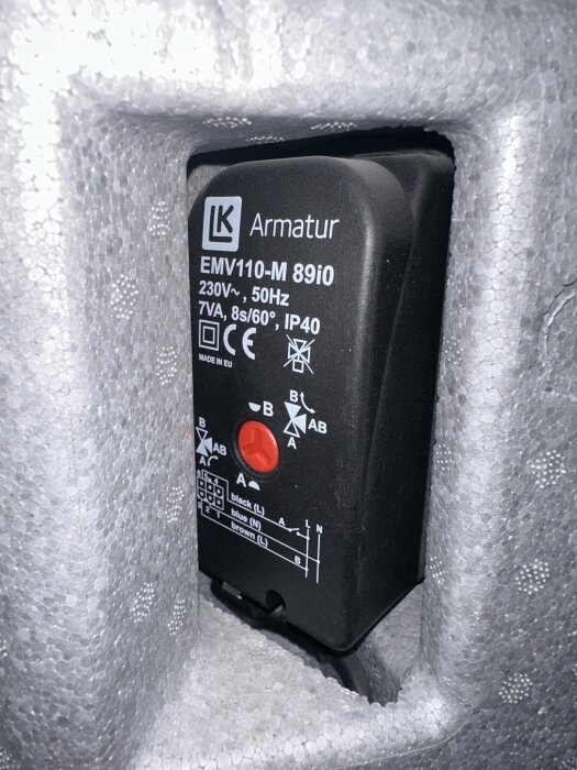 Ventil av märket LK Armatur EMV110-M 89i0 med specifikationer och inkopplingsschema, inbyggd i vad som verkar vara isoleringsmaterial.