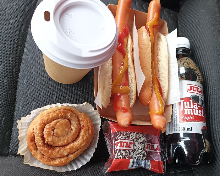 En affärslunch med varmkorv med senap och ketchup, kaffe, kanelbulle, chokladboll och julmust, på bilsäte.