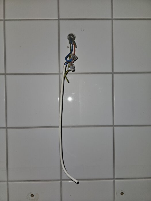 Exponerad strömförande SKX-kabel hänger från vägg på kaklat badrum, borttaget badrumsskåp syns.