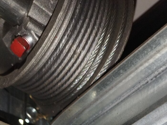 Närbild av en stålvajer lindas runt en metallspole, använd i mekaniska system som garageportöppnare eller hissar.