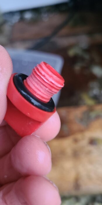 Närbild på en skadad röd plastskruv med gängor, misstänkt tillhörande en AL-KO HW-3000-serie vattenpump.