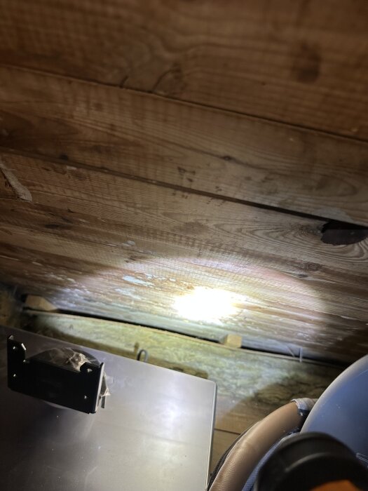Snedtak med träpanel, en del åldringsmärken synliga. En ljuskälla kastar ljus på området. Framför finns en liten svart enhet.