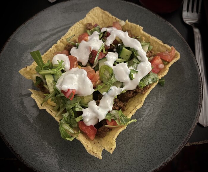 En taco på ett fat med sallad, ost, köttfärs, picklad rödlök, chili, salsa och vitlökssås toppad med färska grönsaker.