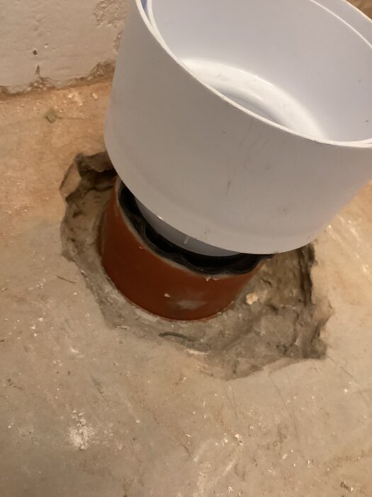 Faluplast WC-anslutning monterad i ett rör med slät ände i golvet, omgiven av betong.