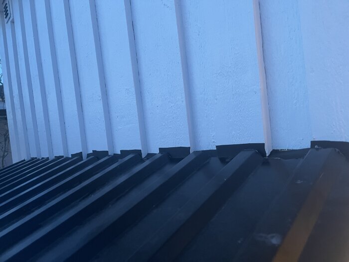 Takavslutning mot en vägg med vita paneler och svart plåttak.