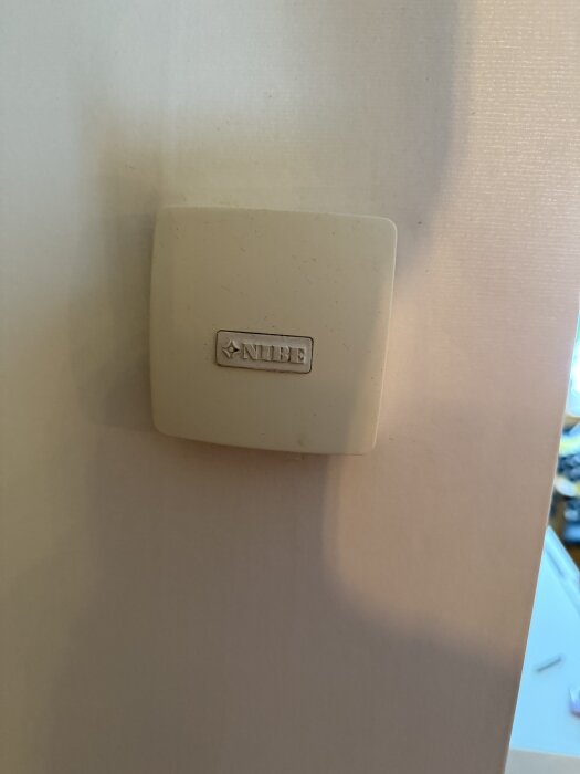 Kontrollenhet för golvvärme märkt "NIBE" monterad på en vit vägg.