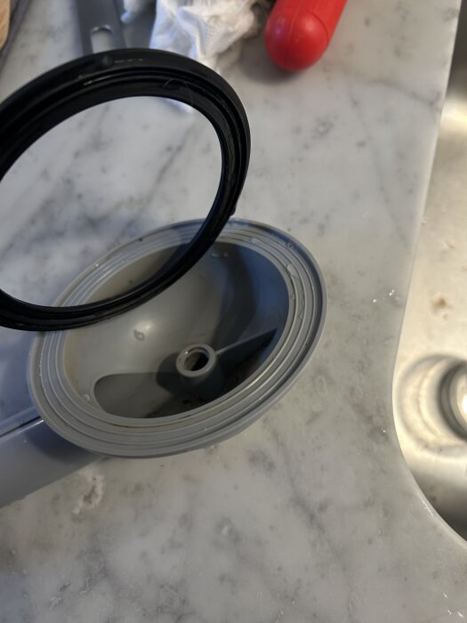 Packning placerad i ett grått rörliggande föremål, fotograferad på en marmorbänk med en röd plastdel i bakgrunden.