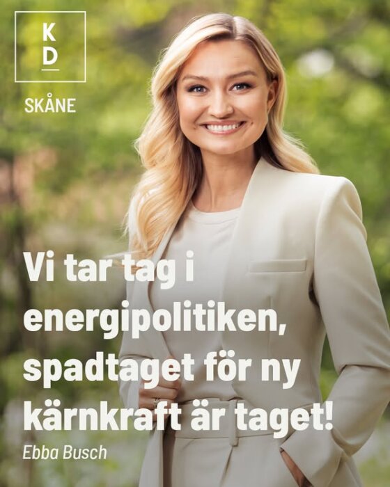 En person i ljus kostym ler framför suddig grön bakgrund med text om energipolitik och kärnkraft från KD Skåne.