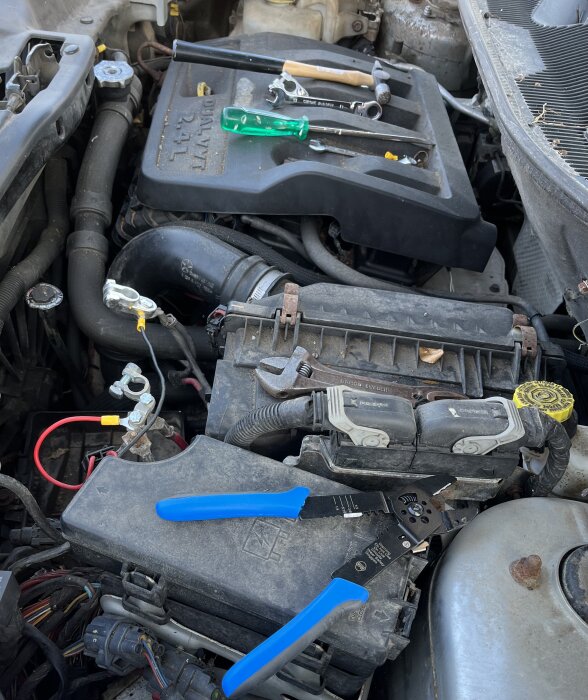 Bilbatteribyte med nya polklämmor, kablar och verktyg placerade på motorn.