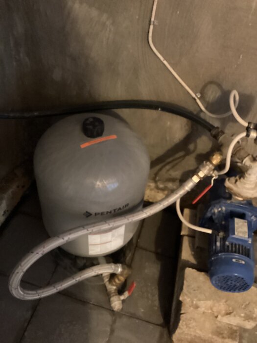 Avhärdningsfilter anslutet till hydroforpump med olika rör, inklusive svart pemslang och blå kulventil, i en källarmiljö.