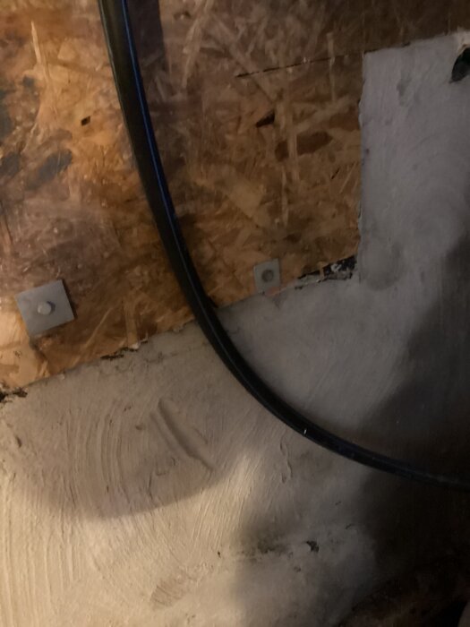 Svart rör mot en träskiva och betongvägg, för inlägg om avhärdningsfilter och pemslanginstallation.