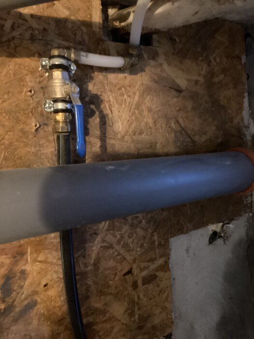 Blå kulventil och kopplingar på en vattenledning, monterad på träpanel, med anslutande rör som del av ett avhärdningsfiltersystem.