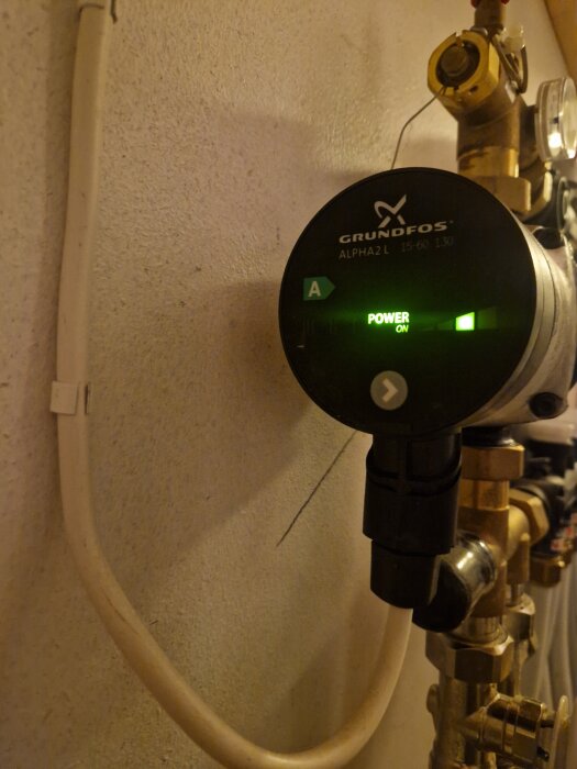 Cirkulationspump Grundfos ALPHA2 L med grönt lysande display, i en rörinstallation, möjligen justerad med ett rött vred.