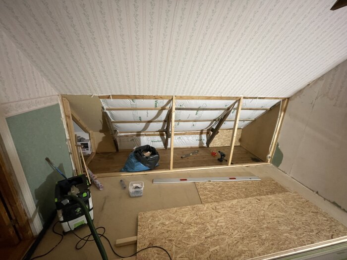 Renovering av sovrum med synliga takstolar och stolpar, verktyg och material på golvet.