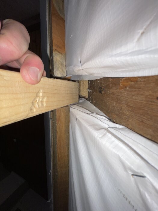 Hand håller en trästolpe mot en takstol i ett rum; isoleringsmaterial syns bakom. Fråga om stolpar kan tas bort under sovrumsrenovering.