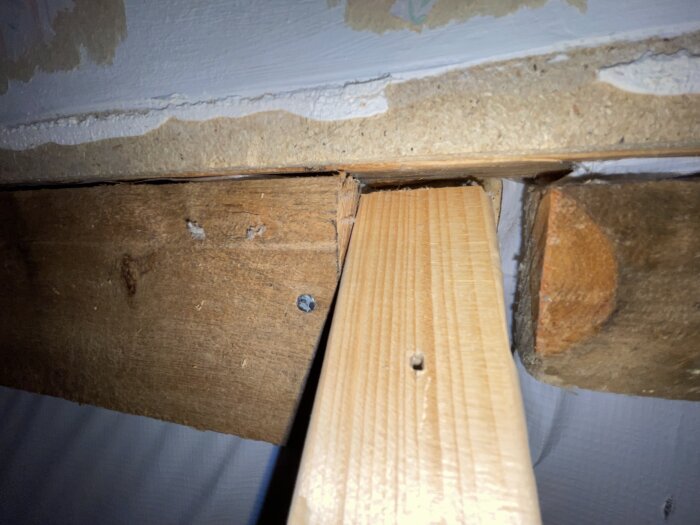 Träkonstruktion med vertikal stödregel mot takstol, med synliga skruvar och trädetaljer, i en pågående renovering av ett sovrum.
