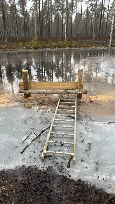 Byggprojekt på frusen sjö, en tillfällig tvärslå och stolpar på isen, stege för viktfördelning. Skog i bakgrunden.