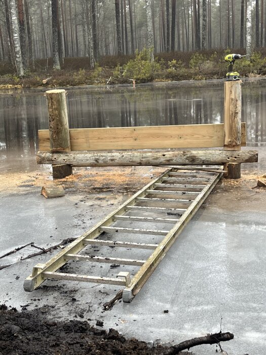 Stege på is vid en bryggkonstruktion med träpelare och verktyg i en skog.