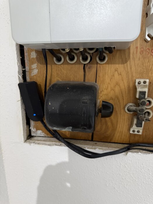 Gammal knivbrytare och elcentral monterad på träskiva med synliga kablar och porslinsproppar, del av diskussion om att byta installationen.