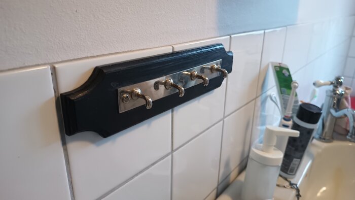 Väggmonterade krokar över kakelvägg, fixerade med dubbelhäftande tejp, i badrumsmiljö nära handfat och hygienartiklar.
