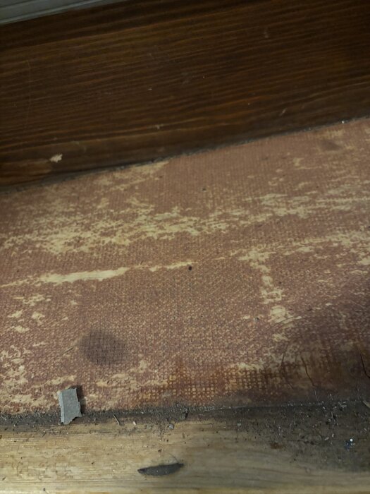 Gammal plastmatta i källartrappa med synligt trä under och rött lim på ytan, troligtvis från 1969.