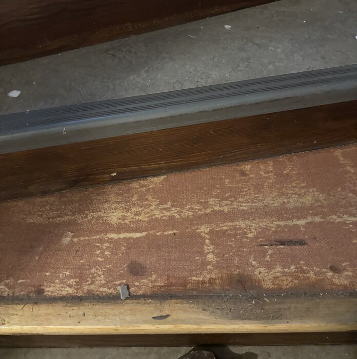 Källartrappa med borttagen plastmatta, trä steg är synliga med kvarvarande rött lim.