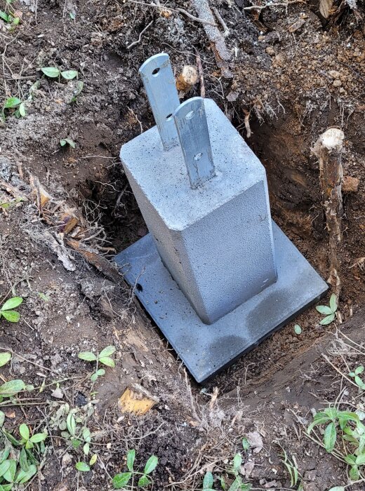 Grå betongplint placerad i en utgrävd grop i marken, omgiven av jord och små växtrester.