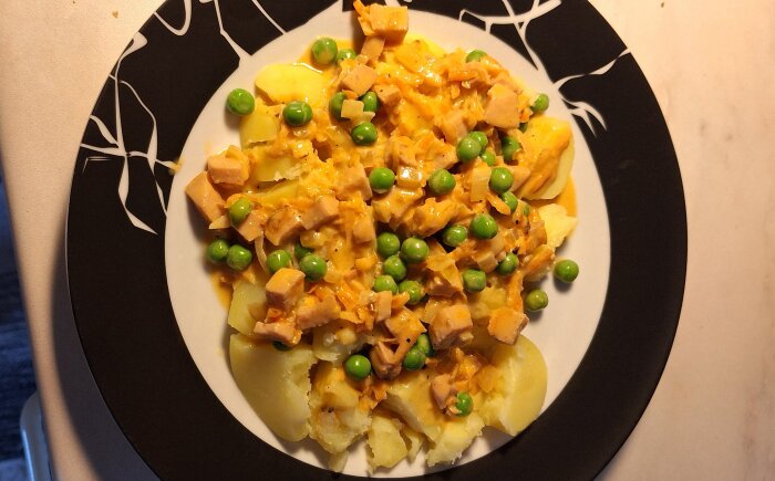 Korv Stroganoff med grovriven morot och ärtor serverad på svartvit tallrik.