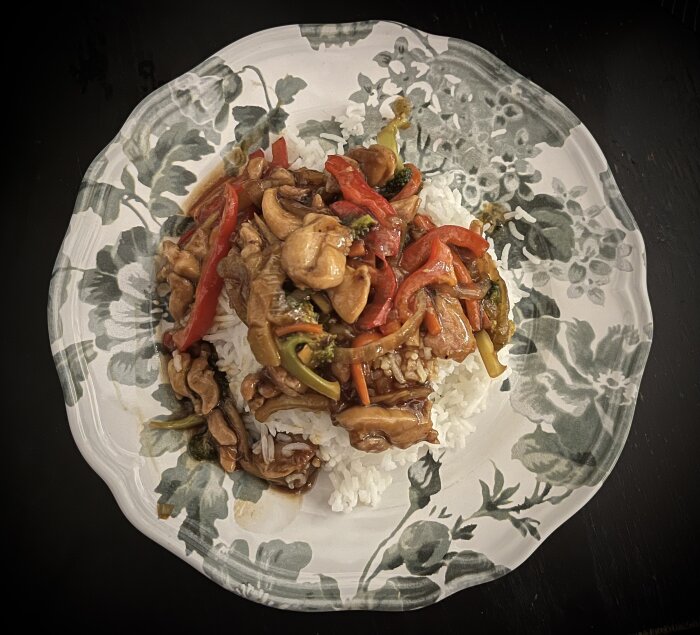 Kyckling med teriyakisås serverad på ris, innehållande lök, morot, broccoli, paprika och bambuskott på en blommig tallrik.