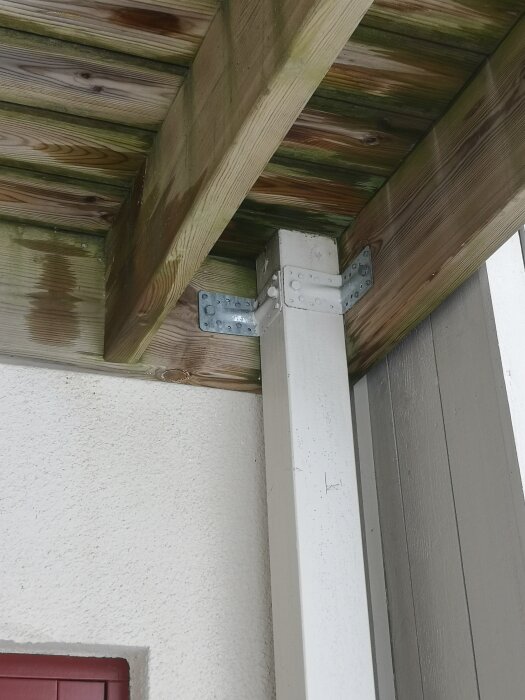 Bilden visar en balkongkonstruktion där träreglar vilar på metallbeslag, monterade på en stolpe. Ramen hänger delvis i skruv utan tydligt stöd på stolparna.