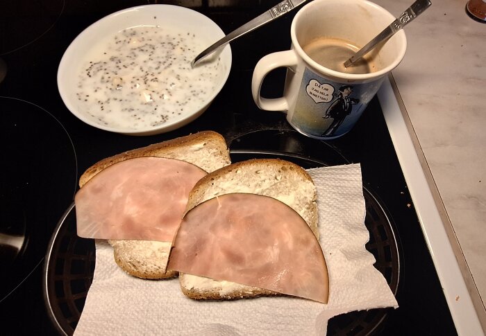 Frukost med yoghurt och chiafrön, två smörgåsar med skinka och en kopp kaffe.