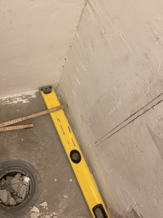 Vägg med vit puts och verktyg som vattenpass och meterstock på golvet, förberett för kakling och montering av duschvägg.