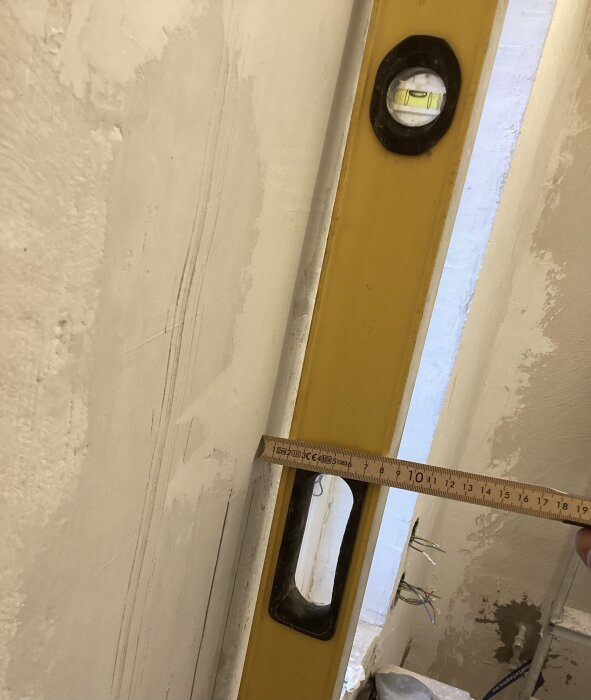 Vattenpass och linjal på ojämn vägg för att bedöma möjlighet att kakla och sätta glasvägg.