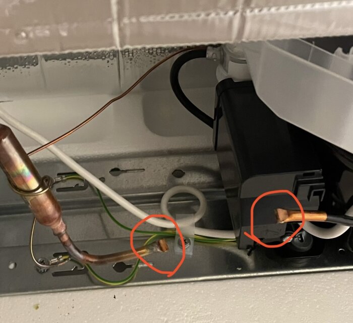 Baksidan av en kyl/frys med synliga kopparrör och anslutningar. Två områden markerade med röda cirklar för kontroll av installationen.