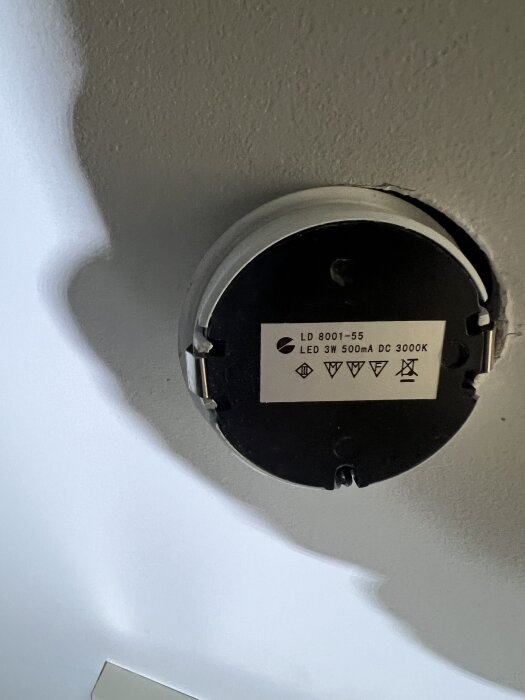Rund LED-enhet monterad i tak med etikett "LD 8001-55, LED 3W 500mA DC 3000K" och olika symboler på en ljus bakgrund.