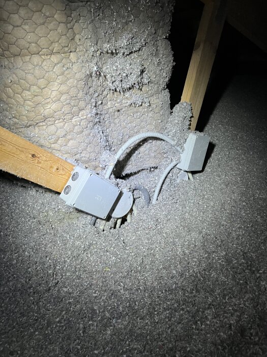 Kabel vid en elbox i isolering på en vind, markerad med ficklampsljus.