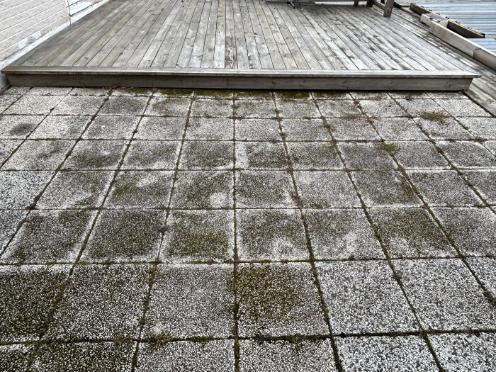 Bilden visar ett befintligt trädäck ovanför en yta av gamla markplattor, del av en diskussion om utbyggnad och byggteknik.