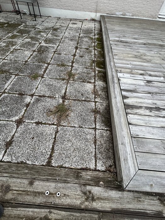 Bilden visar ett befintligt trädäck bredvid gamla betongplattor, med en nivåskillnad synlig i övergången mellan de två ytorna.