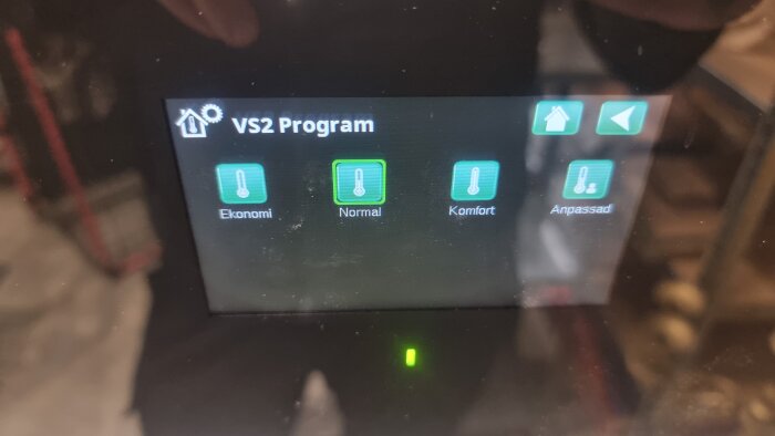 Digital termostat med fyra program: Ekonomi, Normal, Komfort, och Anpassad, visas på skärmen märkt "VS2 Program".