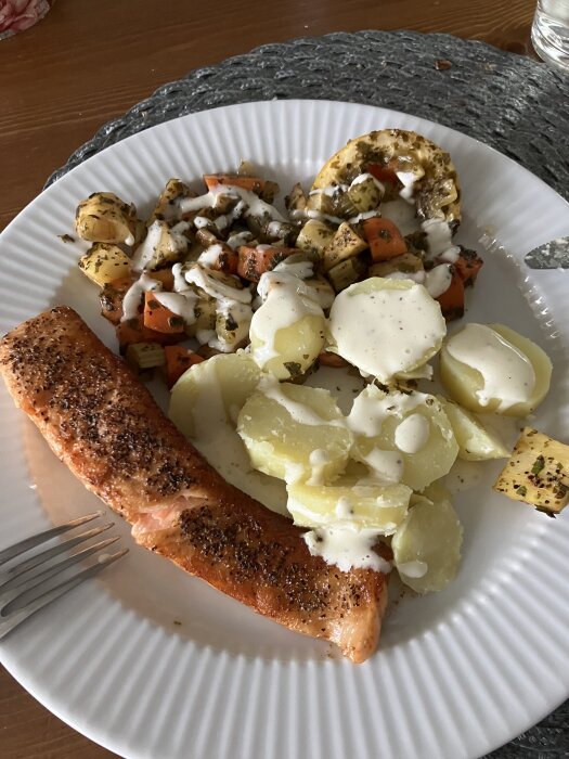 Stekt lax med citronfrästa rotfrukter, kokt potatis och aioli på en vit tallrik.