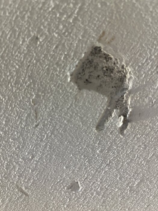 En skadad vit putsad vägg med ett hål och möjligen mögel eller smutsfläckar.