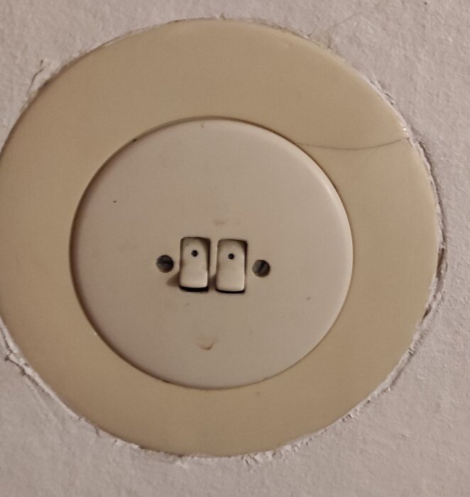 Gammal dubbel strömbrytare i beige på en vägg, avsedd för utbyte mot en modernare variant.